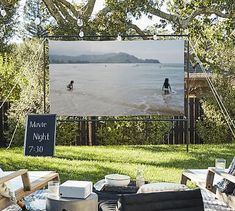 an outdoor movie is set up on the lawn with chairs and tables in front of it