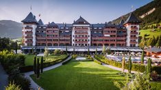 the hotel is surrounded by lush green grass and trees in front of a mountain range