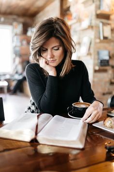 a woman sitting at a table with an open book and cup of coffee