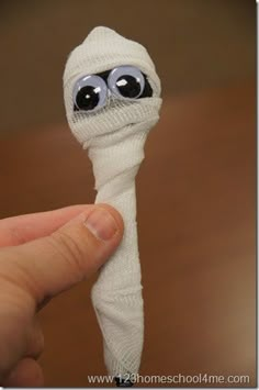 a hand holding a small white object with eyes on it's head and wrapped in yarn