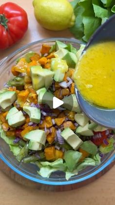 a person pouring dressing into a salad in a glass bowl with lettuce and tomatoes on the side