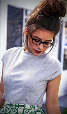 a young woman wearing glasses and a white shirt is looking down at her cell phone