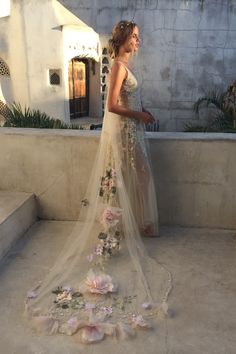 a woman in a wedding dress with flowers on the ground next to her, looking off into the distance