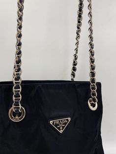 A black Prada nylon tote with silver chain to be over the shoulder. The silver chain has black leather threaded through with a black leather piece at the top, for comfort when wearing. Inside the bag is lined with the famous Prada logo nylon lining. There is a middle zipped compartment and a further interior zipped pocket for valuables. The bag is in good vintage condition and comes with its original Prada dust bag. Prada Nylon Tote, Prada Nylon, Prada Logo, Leather Thread, Nylon Tote, Leather Pieces, Vuitton Bag, Diaper Backpack, Casual Backpack