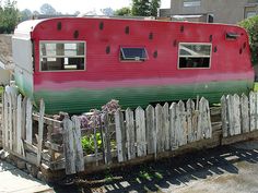 a red and green trailer parked next to a wooden fence in front of a house