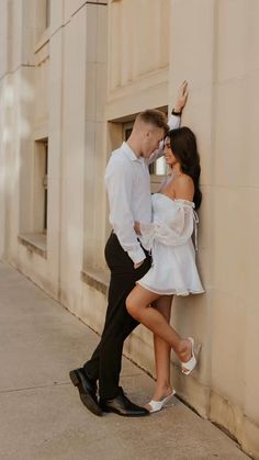 a man and woman leaning against a wall in front of a building with their arms around each other