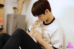 a young man holding a cat in his lap while sitting on the floor next to a book shelf