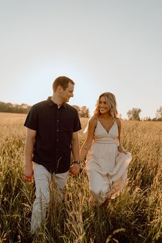 a man and woman holding hands walking through tall grass