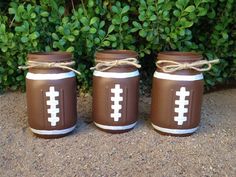 three mason jars decorated with brown and white footballs are sitting in front of some bushes