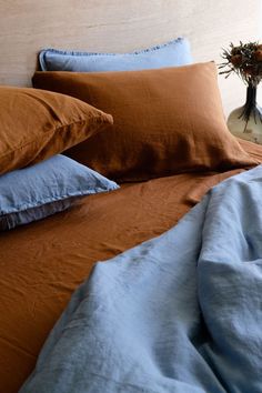 a bed with blue and brown sheets, pillows and a vase filled with flowers on it