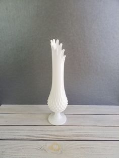 a white vase sitting on top of a wooden table next to a gray wall in the background