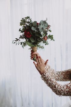 a woman holding a bouquet of flowers up to her face in front of a curtain