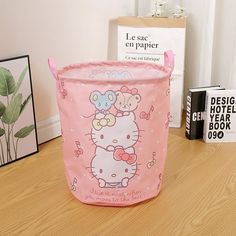 a pink hello kitty storage basket sitting on top of a wooden floor next to books