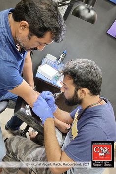 two men in blue shirts and gloves are doing something on someone's hand while another man looks at the camera