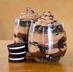 two desserts in glasses with cookies and oreo cookies on the table next to them