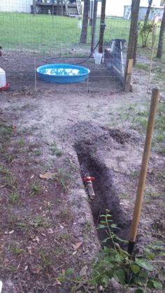 an open hole in the ground next to a fence with a blue swimming pool behind it