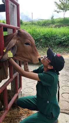 a woman in green jumpsuits petting a cow