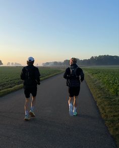 two people running down a road in the middle of a field at sunset or sunrise