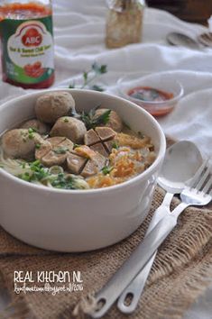 a white bowl filled with food on top of a table next to utensils