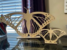 two paper butterflies sitting on top of a glass table next to a pencil holder and window