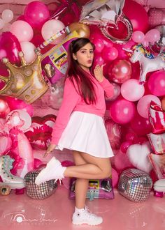 a woman in pink shirt and white skirt standing next to balloon filled wall with balloons