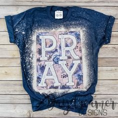 a t - shirt with the word pray printed on it, sitting against a wooden background