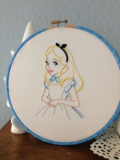 a white and blue embroidery on a wooden table next to a doily with a drawing of a girl