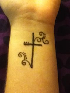 a small tattoo on the wrist of a woman with a cross and swirls around it