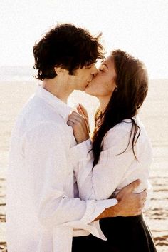 a man and woman kissing each other while standing next to the ocean in black and white