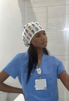 a woman in scrubs standing next to a white wall and looking at the camera