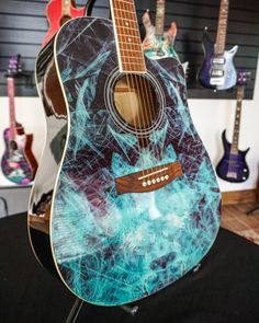 an acoustic guitar is painted with blue and black swirls on the top, while other guitars are in the background