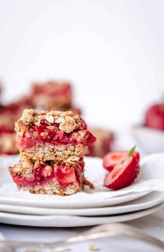 strawberry crumble bars stacked on top of each other with strawberries in the background