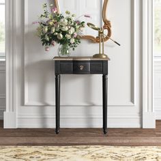 a black table with flowers on it in front of a white wall and a gold framed mirror