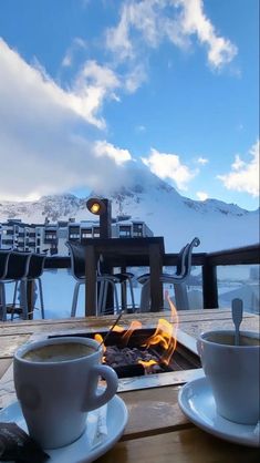 two cups of coffee sitting on top of a wooden table next to a fire pit