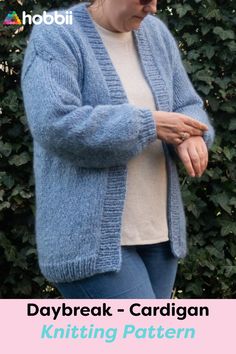 a woman wearing a blue cardigan standing in front of a bush with text overlay that reads, daybreak - cardigan knitting pattern