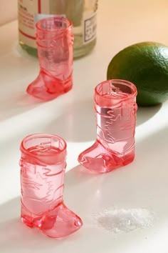 three pink glass cups sitting on top of a table next to a lime and bottle