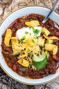 a white bowl filled with chili, beans and sour cream on top of a wooden table