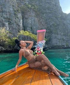 a woman laying on top of a wooden boat in the ocean next to mountains and cliffs