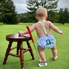 a baby in diapers standing next to a wooden stool with a golf club on it