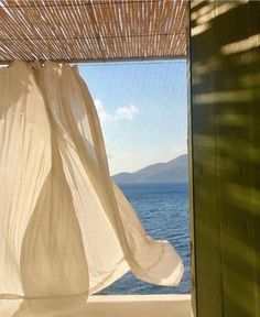 an open window with sheer curtains over the water