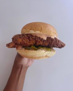 a hand holding up a chicken sandwich with pickles