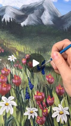 someone is painting flowers in the field with mountains in the backgroound and clouds in the sky