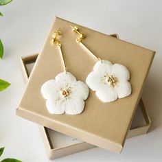 two white flower earrings sitting on top of a box