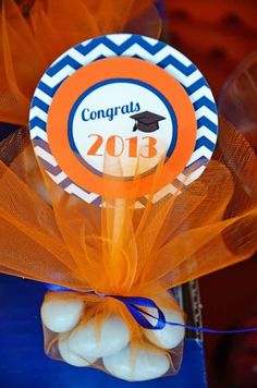 an orange and blue graduation decoration on top of a table with some candy in it