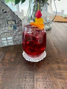 a glass filled with red liquid on top of a wooden table next to a potted plant