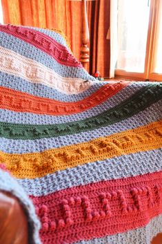 a crocheted blanket sitting on top of a couch next to a wooden chair