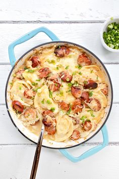 a skillet filled with pasta and sausage on top of a white wooden table next to a bowl of peas