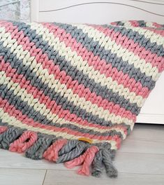 a crocheted blanket laying on top of a wooden floor next to a bed