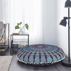 a living room with a large round floor pillow on the floor next to a lamp