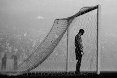 a man standing in front of a soccer goal with his head on the net while people watch